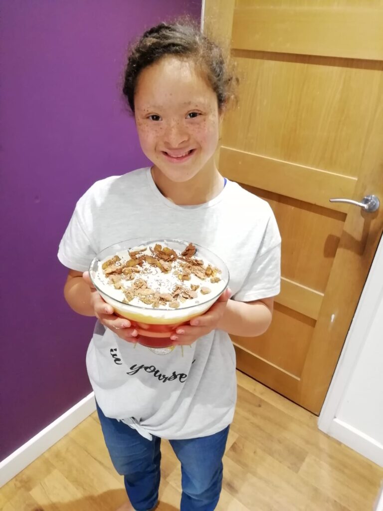 Ruby, wearing a white shirt and holding a cake while smiling happily at the camera
