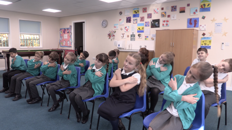 A class of children, all crossing their arms, doing an exercise that promotes good attachment