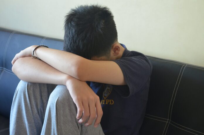 A teen boy with his head in his arms, wearing a shirt that says 'NYPD'