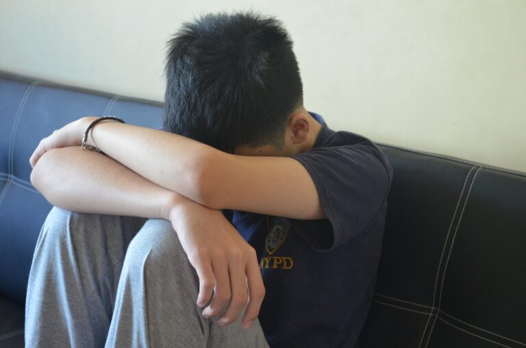 A teen boy with his head in his arms, wearing a shirt that says 'NYPD'